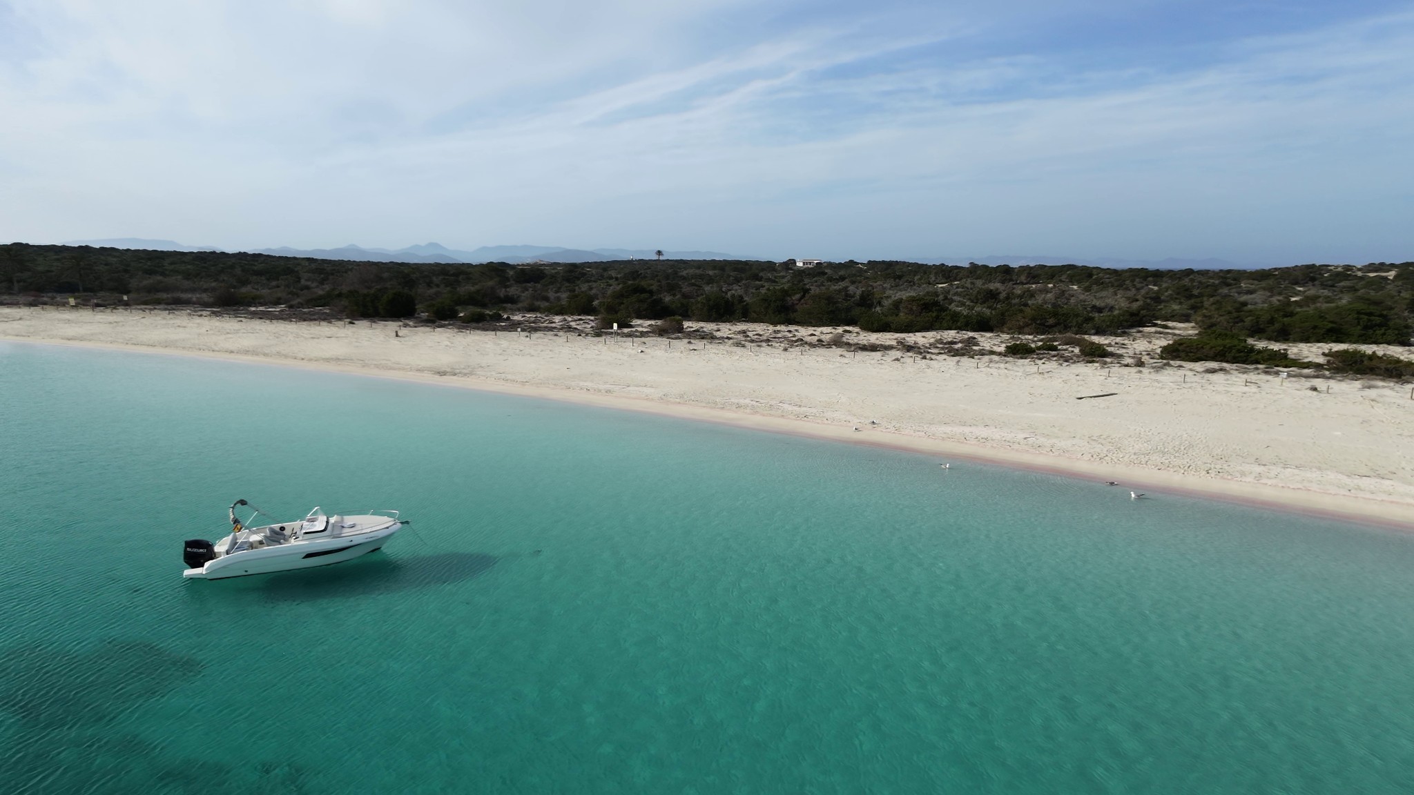 Buena Proa anchored in clear waters with a beach in the background